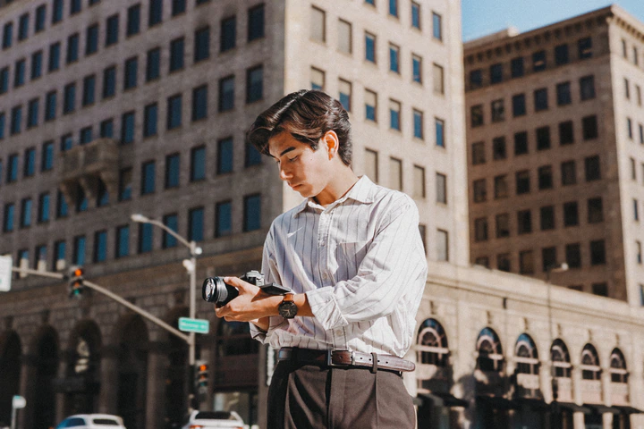 Kai looking down at his camera on a downtown street corner