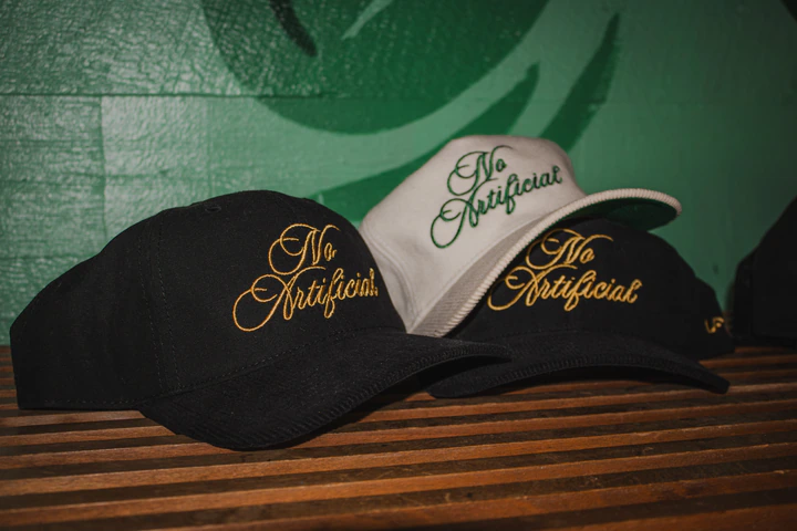Black and white caps embroidered No Artificial on a wooden bench