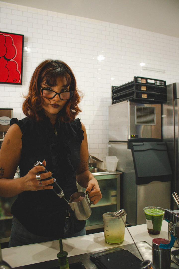 Barista frothing milk, looking at the camera
