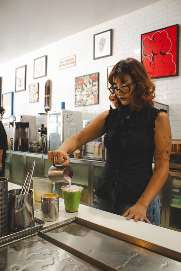 Barista pouring strawberry cold foam over an iced matcha